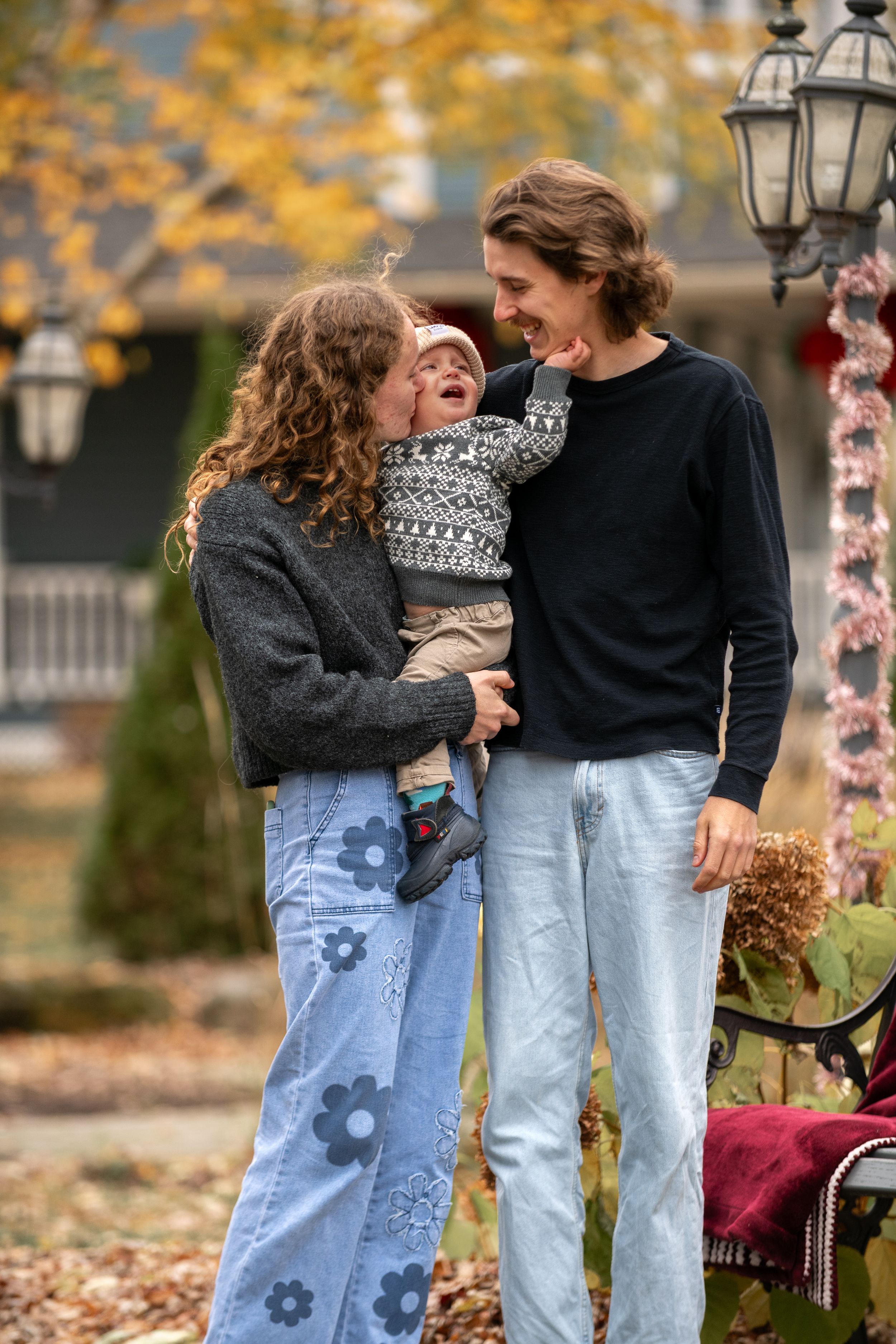 A couple wearing matching jeans and sweaters share a candid moment together in a park during autumn.