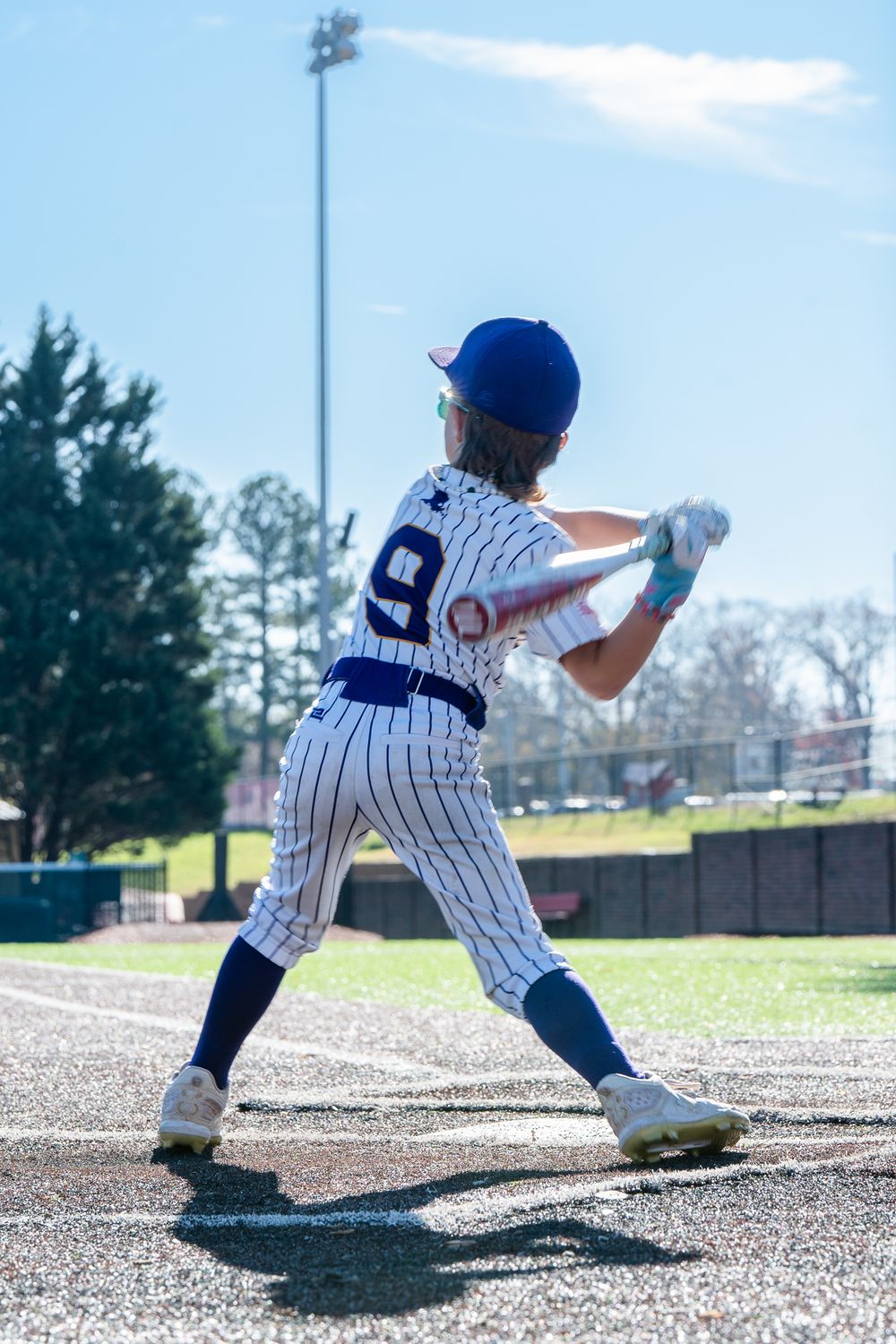 Baseball player in pinstriped uniform and blue cap takes batting stance on field during sunny day.
