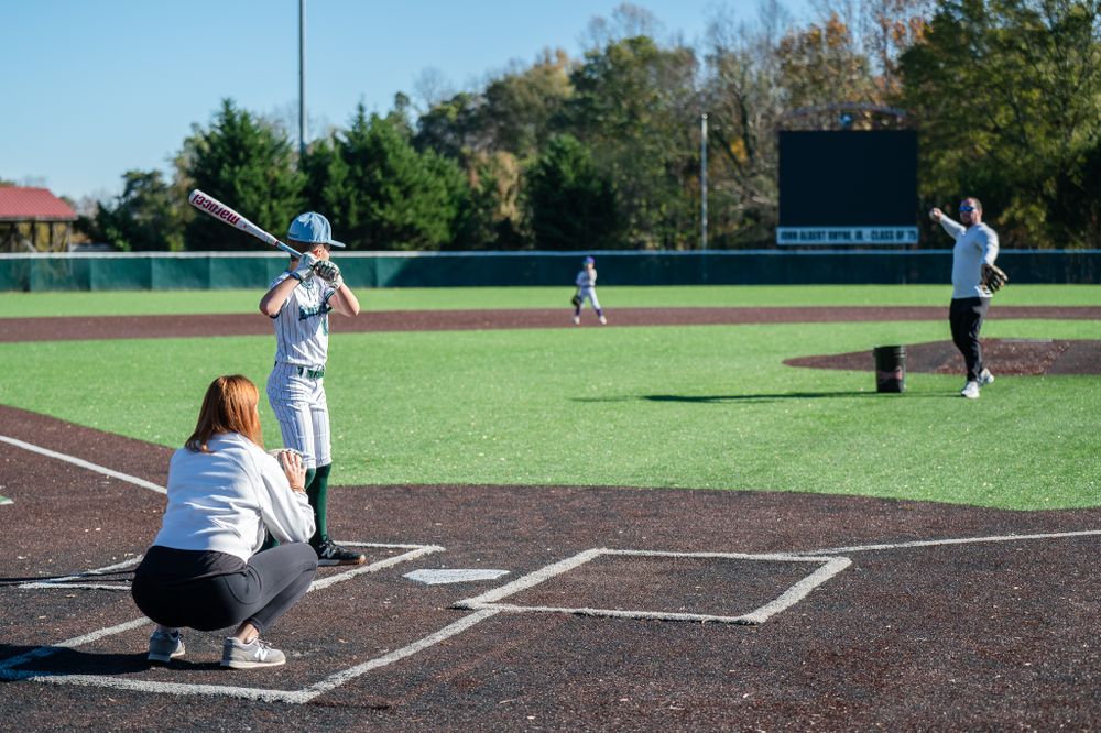Baseball players practicing on field with catcher crouching behind home plate.