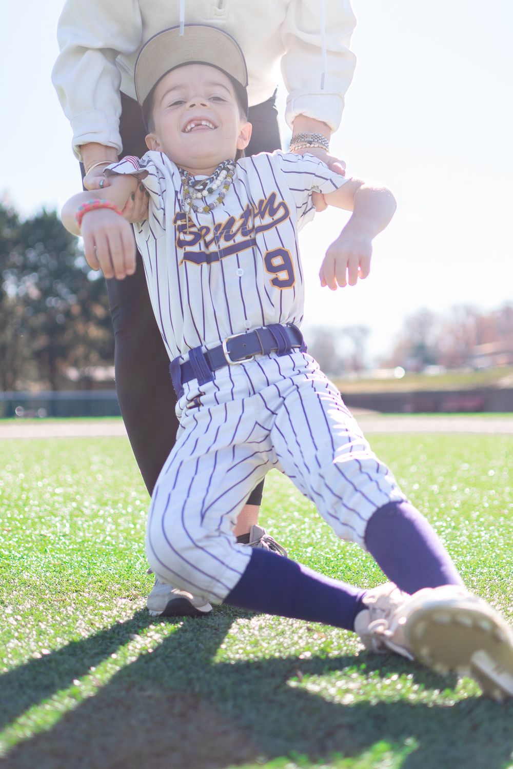 Youth baseball player in pinstriped uniform stretches during practice on sunny field.