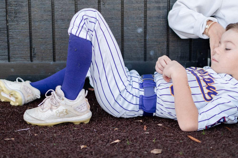 Baseball cleats and striped uniform pants lying on a red dirt field.