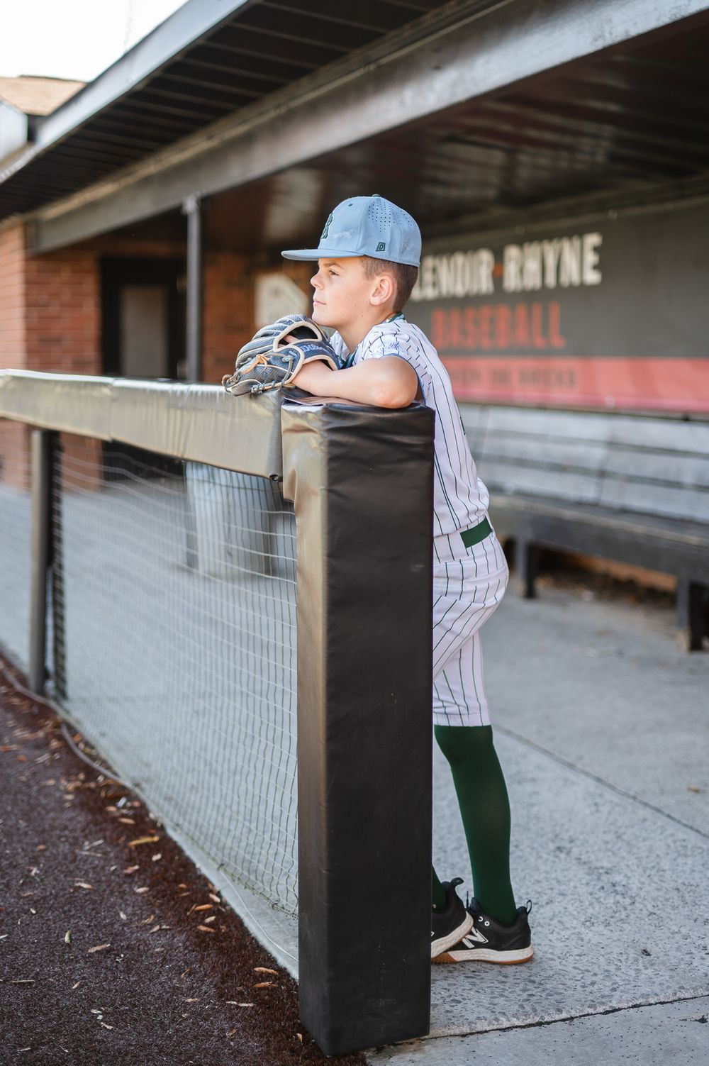 Young baseball player in uniform leaning on dugout railing.