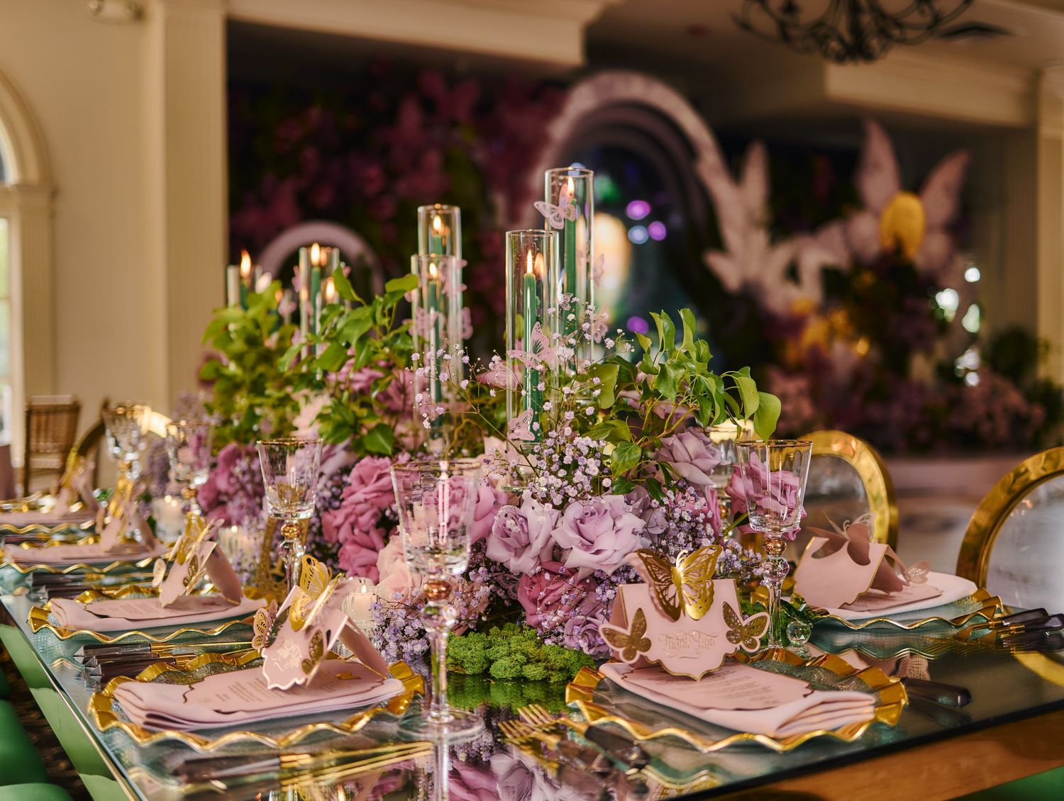 Elegant dining table set with pink and purple floral centerpieces, crystal candlesticks, and formal place settings.