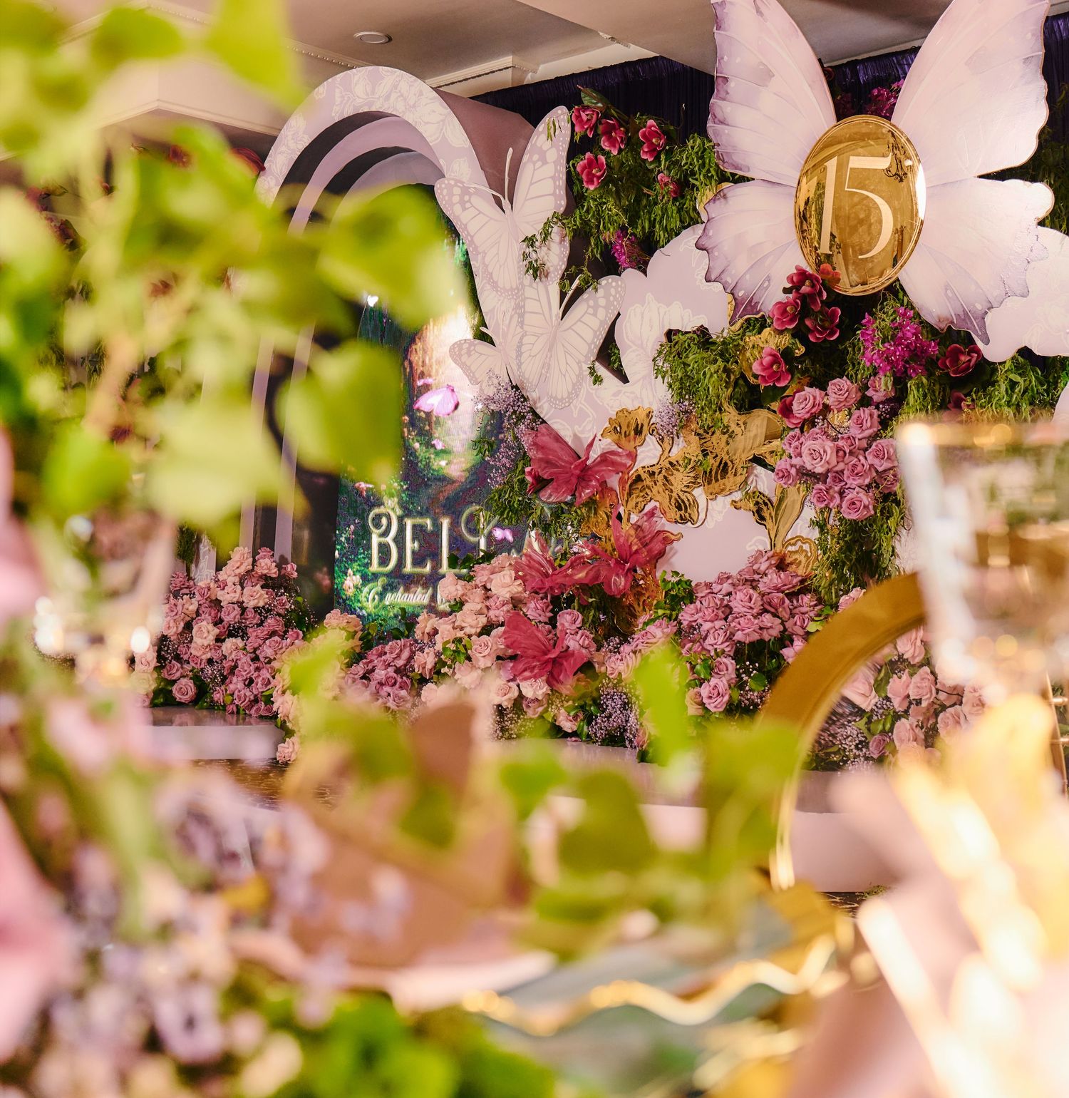 Pink floral decorations with white angel wing props and sparkling party decor create an ethereal celebration display.
