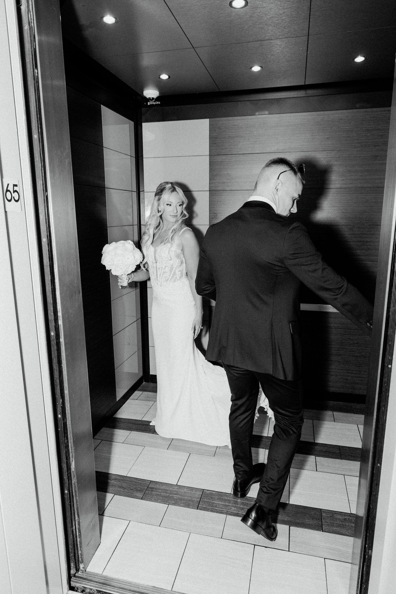 Black and white wedding photo of couple in elevator with bride holding bouquet.