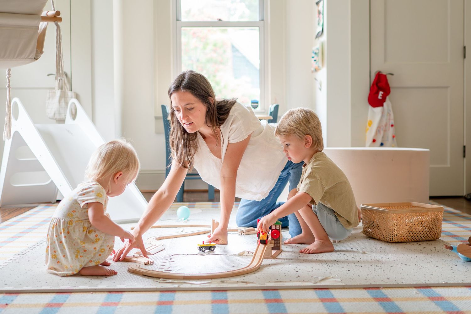 Three people play together on a light-filled floor with a round shaped toy in a bright interior room.