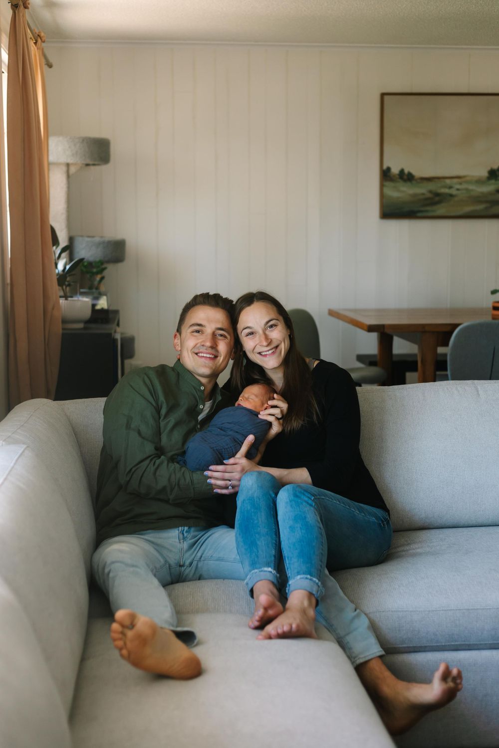 A couple cuddling on a gray couch in a cozy living room with landscape art on the wall.