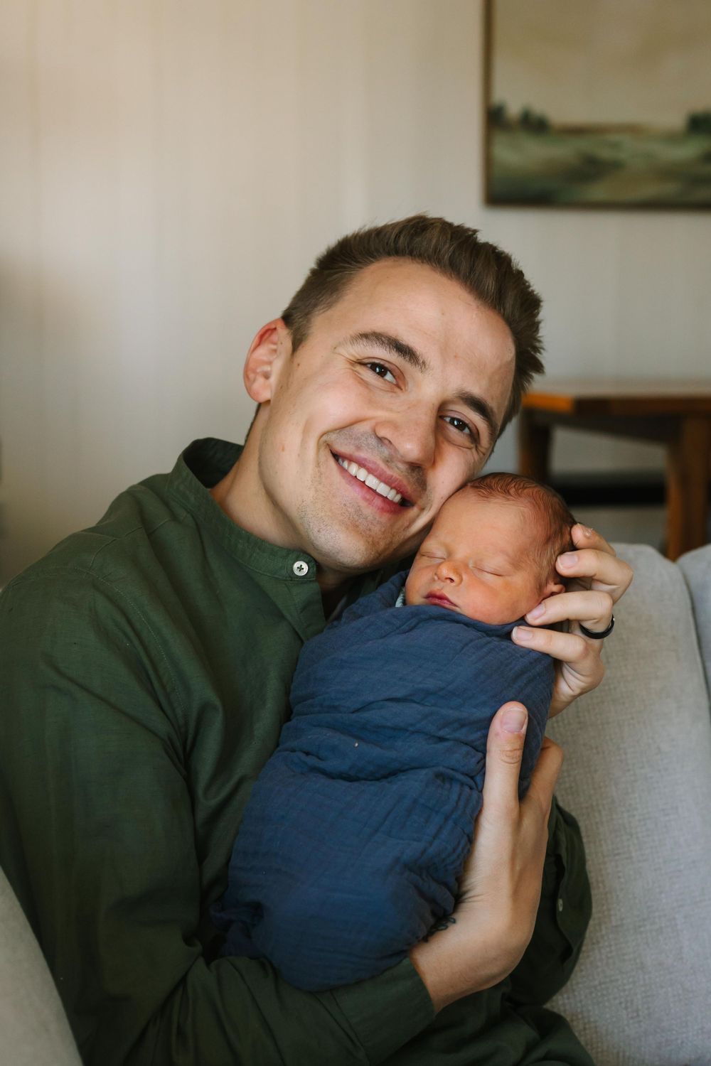 A newborn baby in blue swaddle being held on a cozy gray couch.