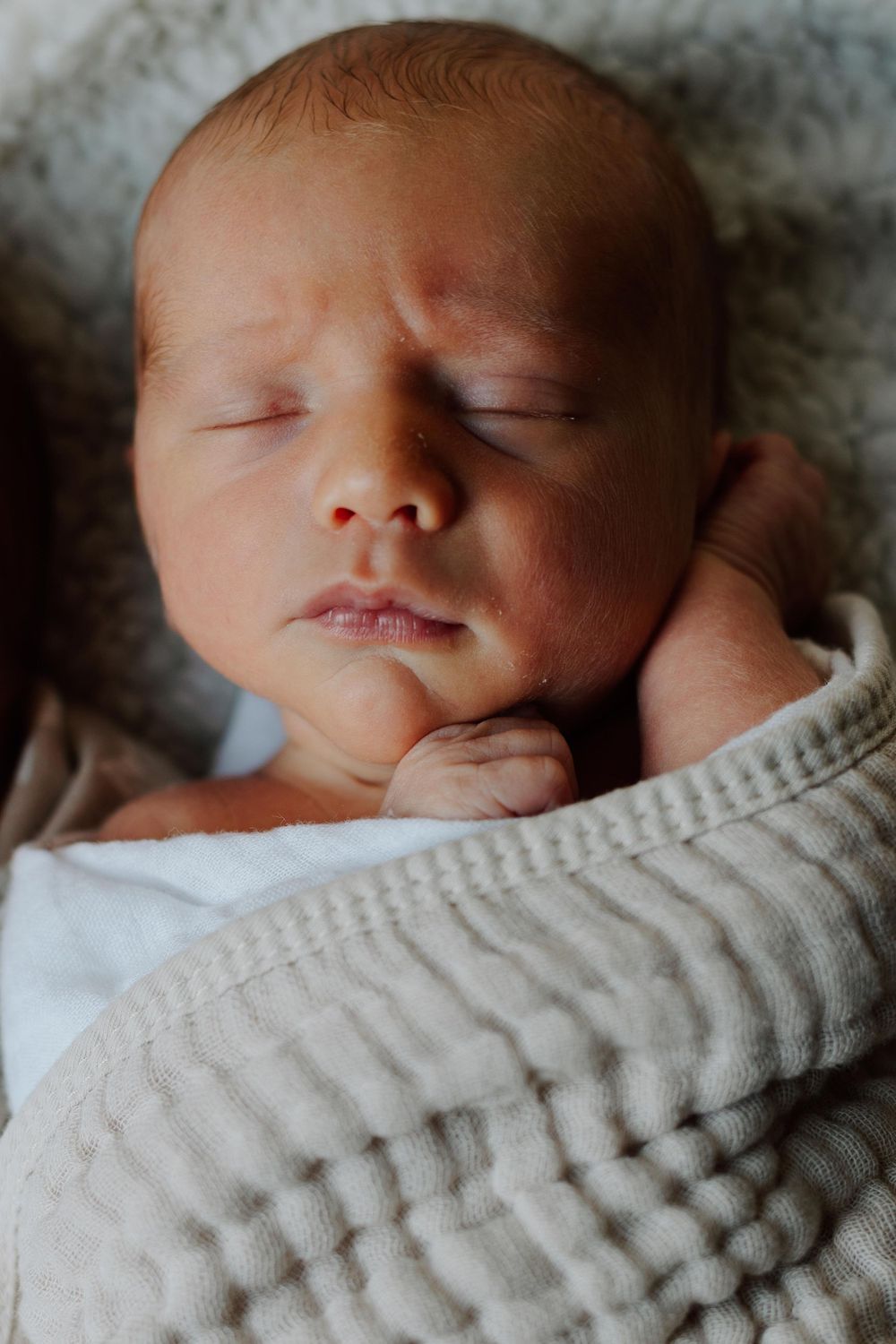 A peaceful sleeping newborn baby swaddled in a soft gray blanket against a neutral background.