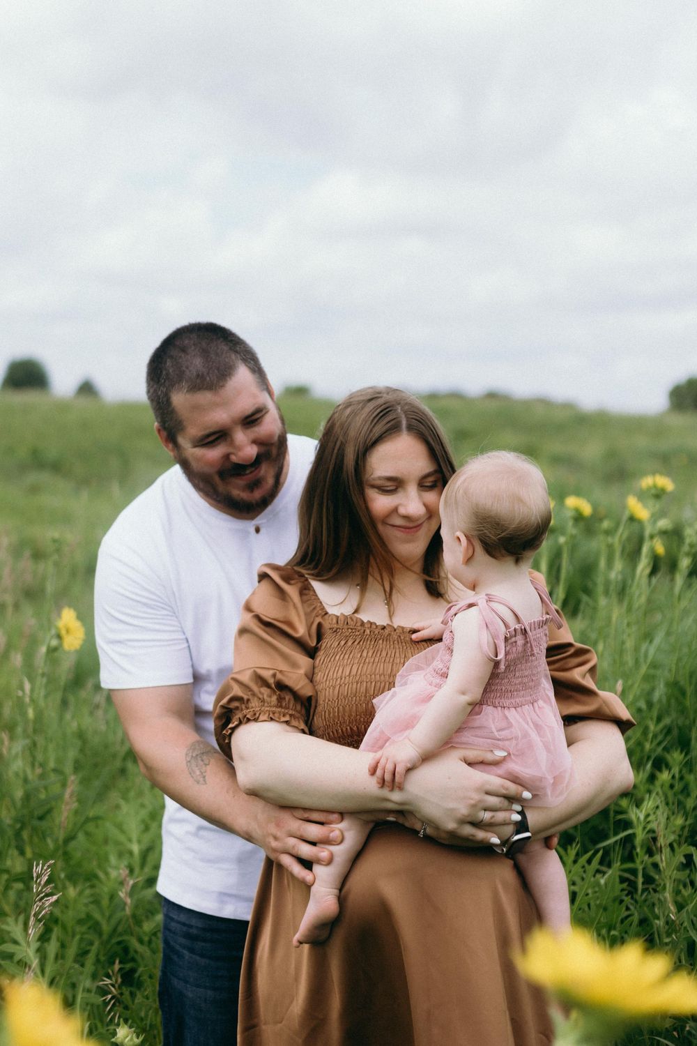Happy family laughing together while standing in meadow with blooming yellow flowers.