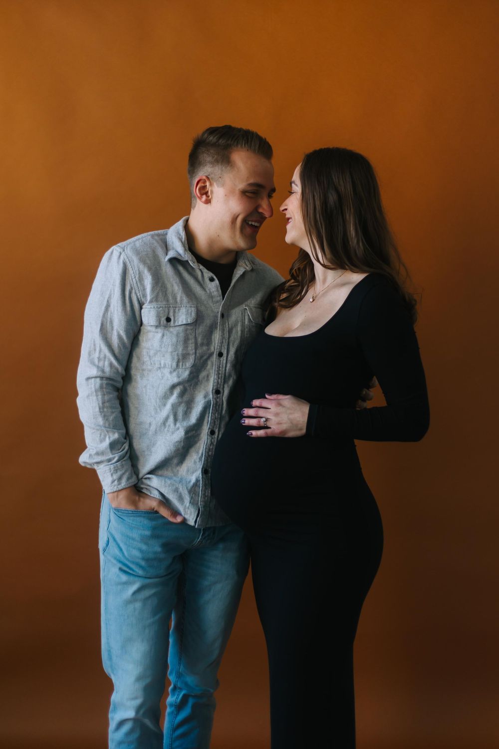 Intimate maternity portrait of couple sharing tender moment against warm orange wall.