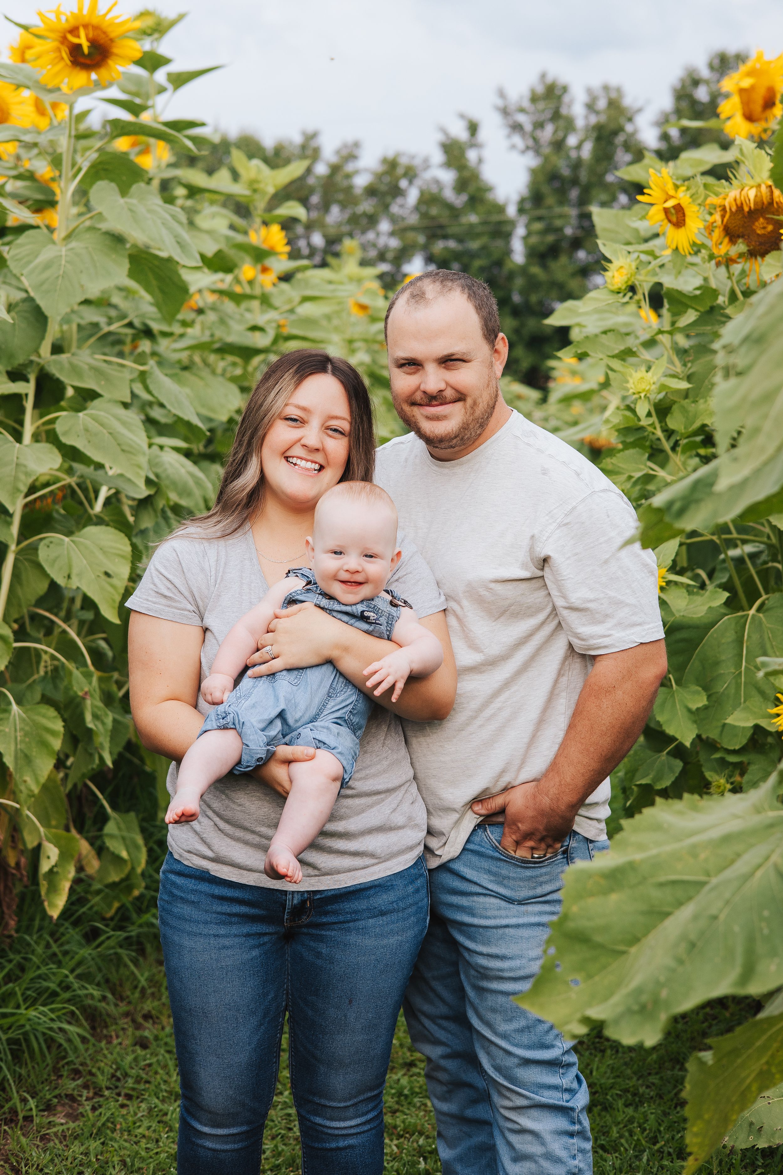 Family poses together in a sunflower field wearing casual clothing on a summer day.