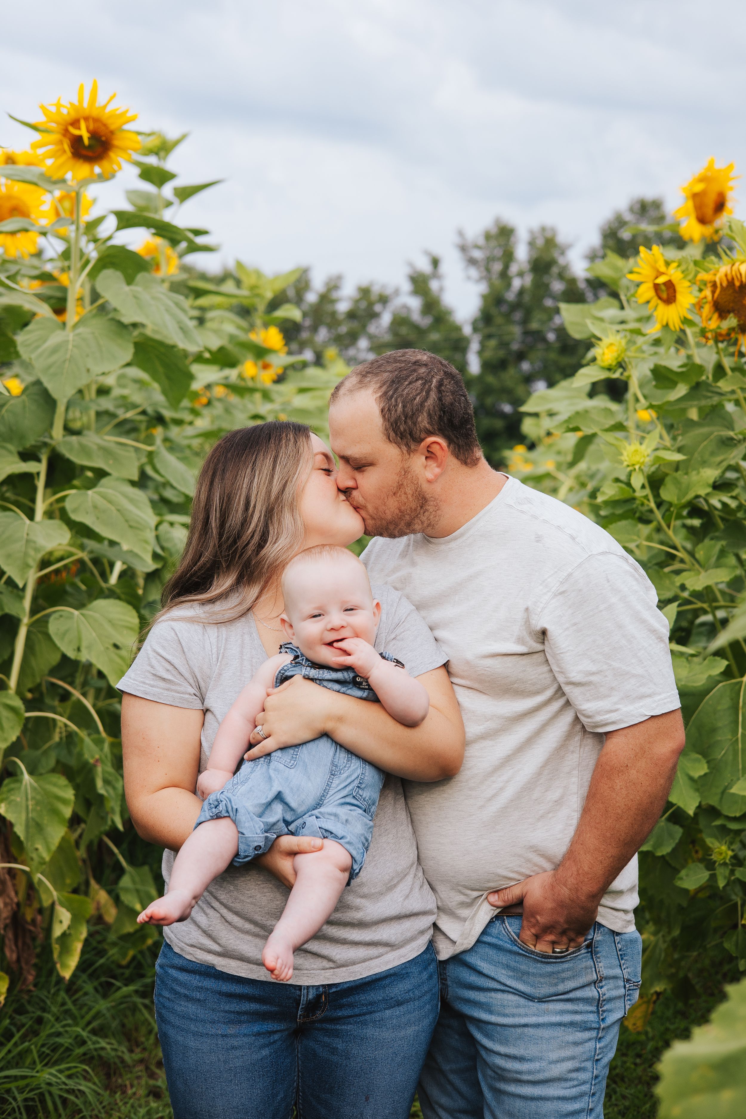 Tender family moment captured among blooming sunflowers on a bright day.
