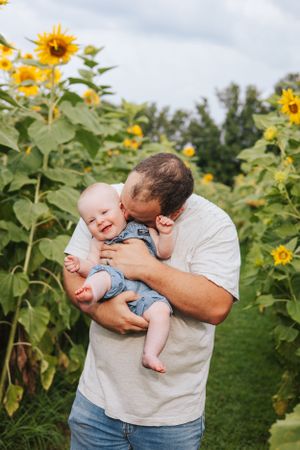 Playful interaction with baby among rows of sunflowers.