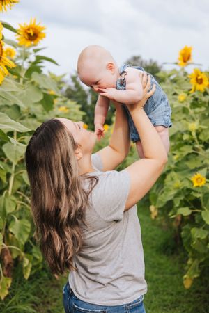 Parent lifting baby high in the air among blooming sunflowers.