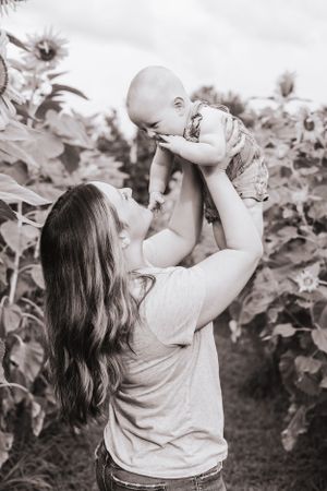 Black and white photo of parent lifting baby against sunflower backdrop.