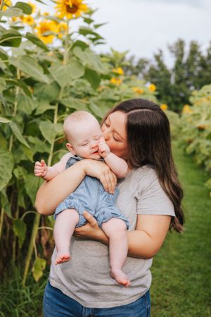 A tender moment between parent and infant surrounded by blooming sunflowers in a garden setting.