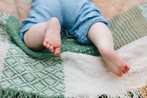 Small bare feet with painted toenails resting on patterned blanket outdoors.