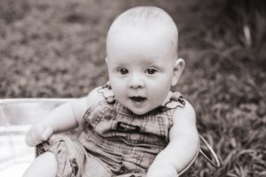 Black and white portrait of a baby in denim overalls sitting up.