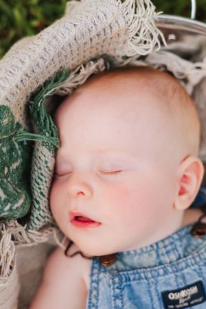 Close up of a sleeping baby wearing denim overalls and a knit hat outdoors.
