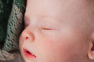 Close-up profile view of sleeping baby's peaceful face against woven texture.
