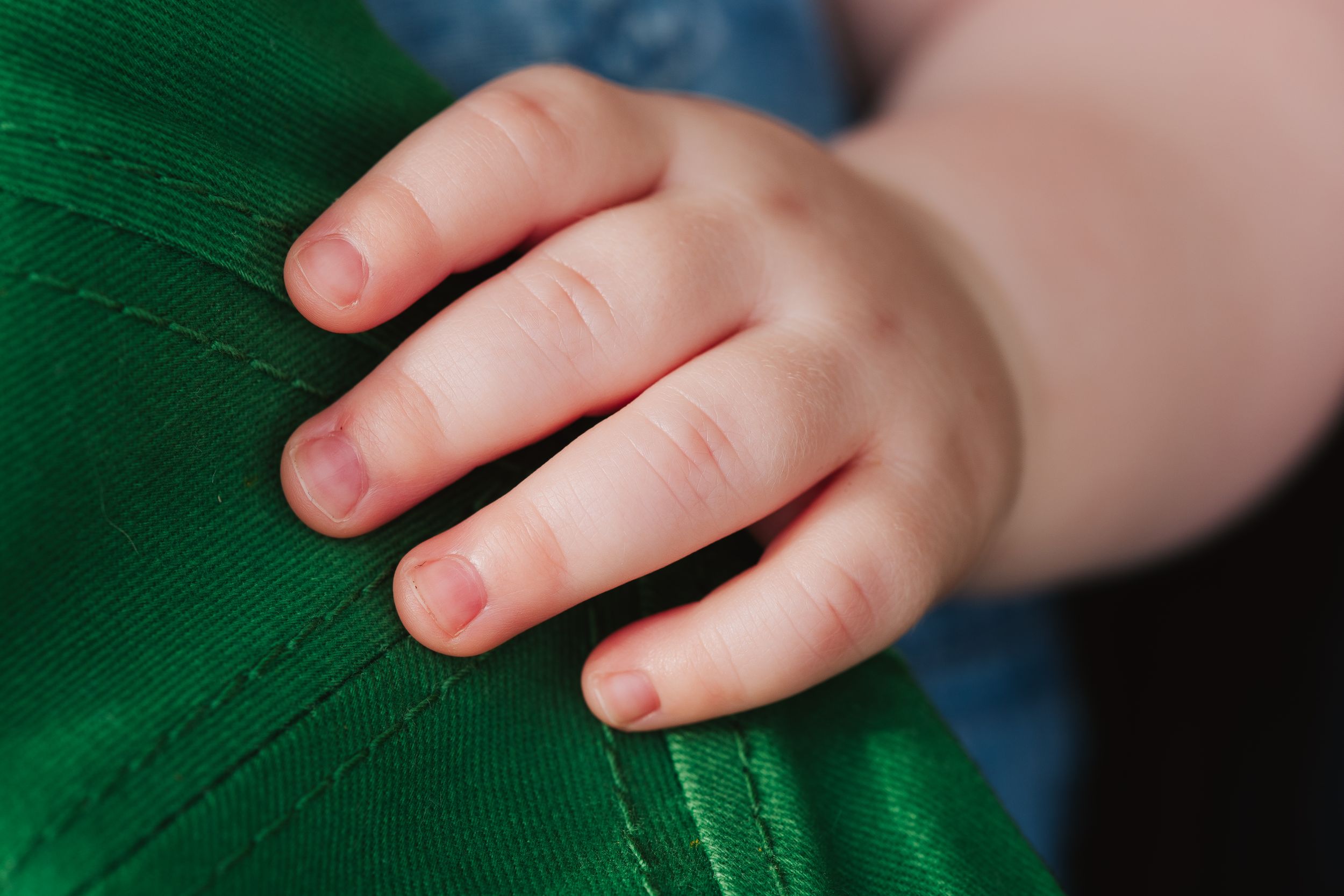 Small hand grasping green fabric showing delicate baby fingers and texture.
