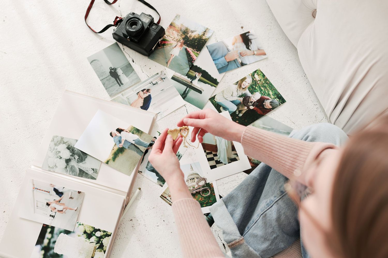 Hands arrange vintage photographs scattered on a white surface next to a film camera in a nostalgic display.