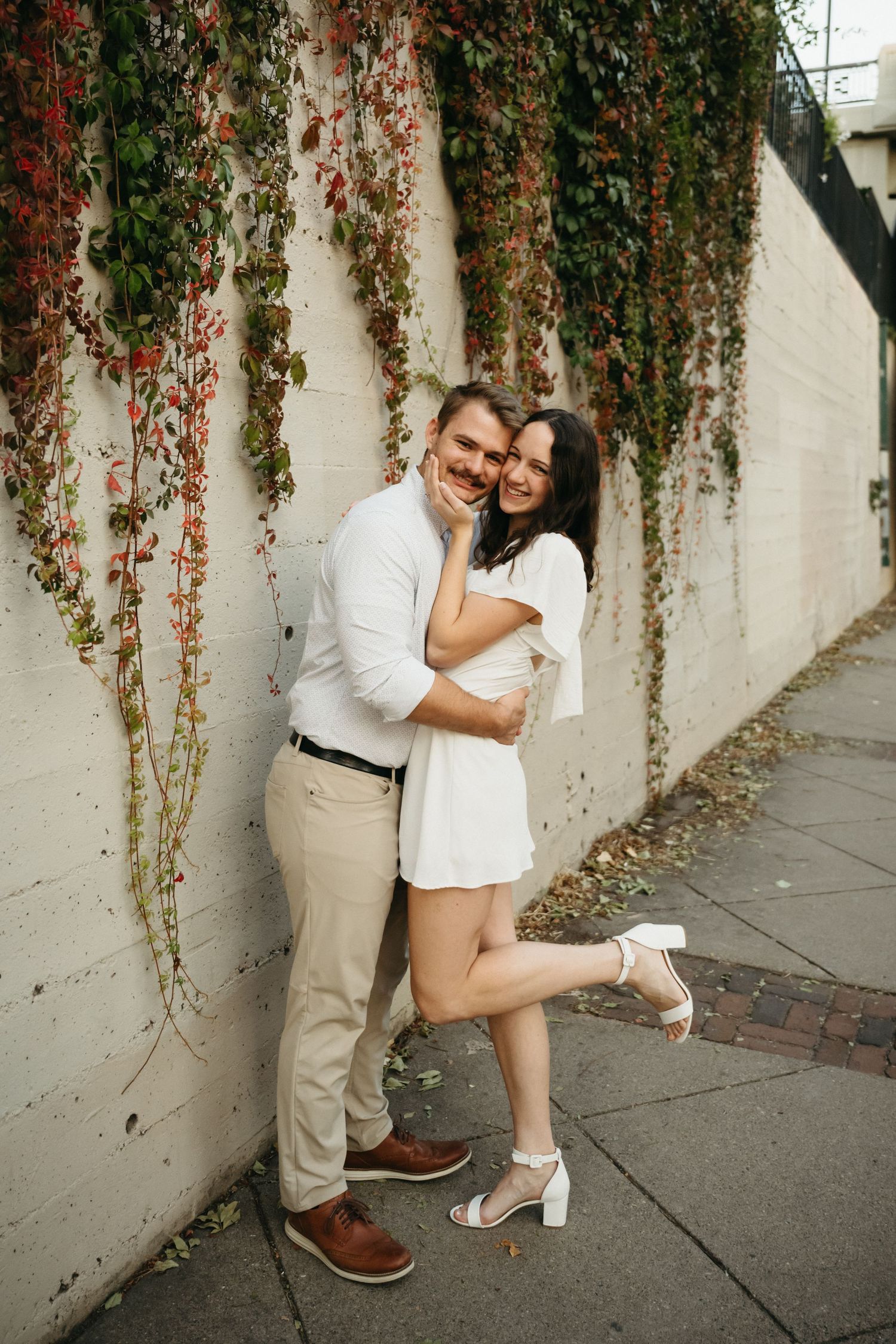 A couple embracing against a wall covered in red and green ivy vines.