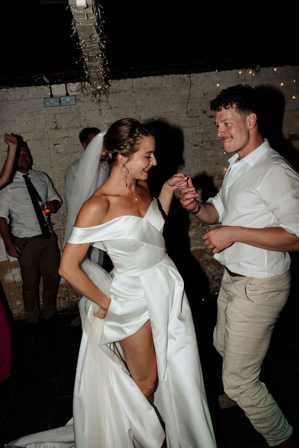 A bride and groom dance on the dancefloor after their wedding ceremony surrounded by their friends drinking wine.