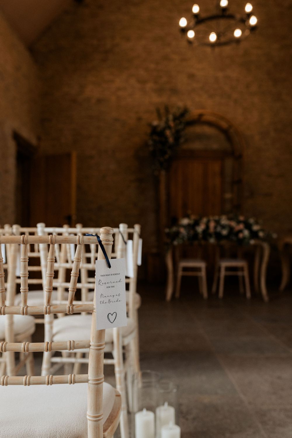 White wooden chairs arranged in rows for a wedding ceremony in a rustic stone venue with floral arch decor.