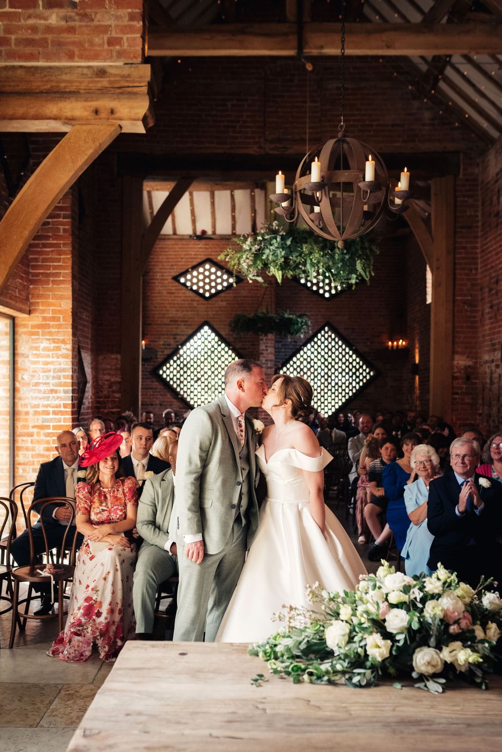A newly married couple share a first kiss in front of all their wedding guests, inside a barn conversion wedding venue.