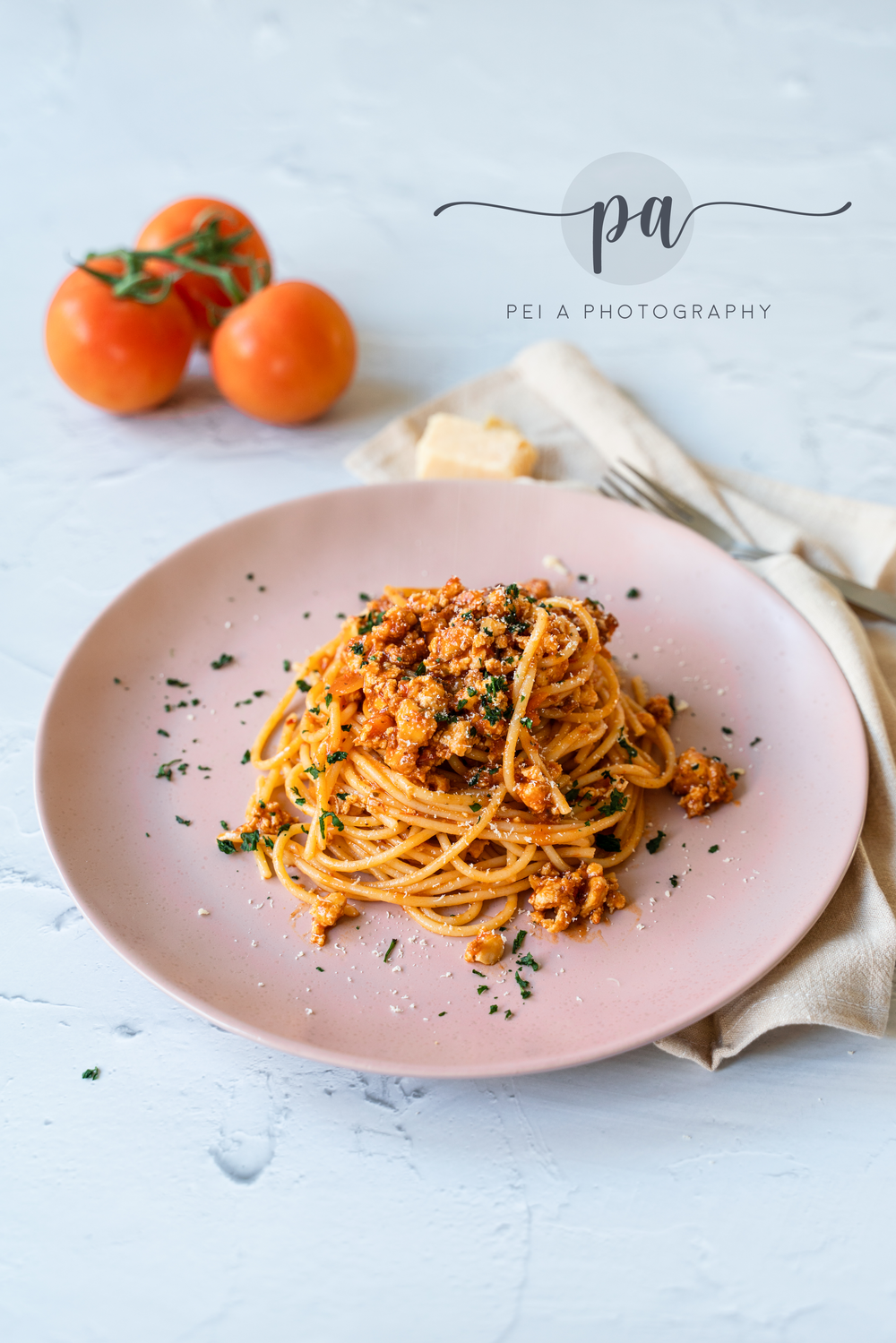 Fresh pasta with tomato sauce on pink plate next to cherry tomatoes on marble surface taken by Melbourne food styling photographer.