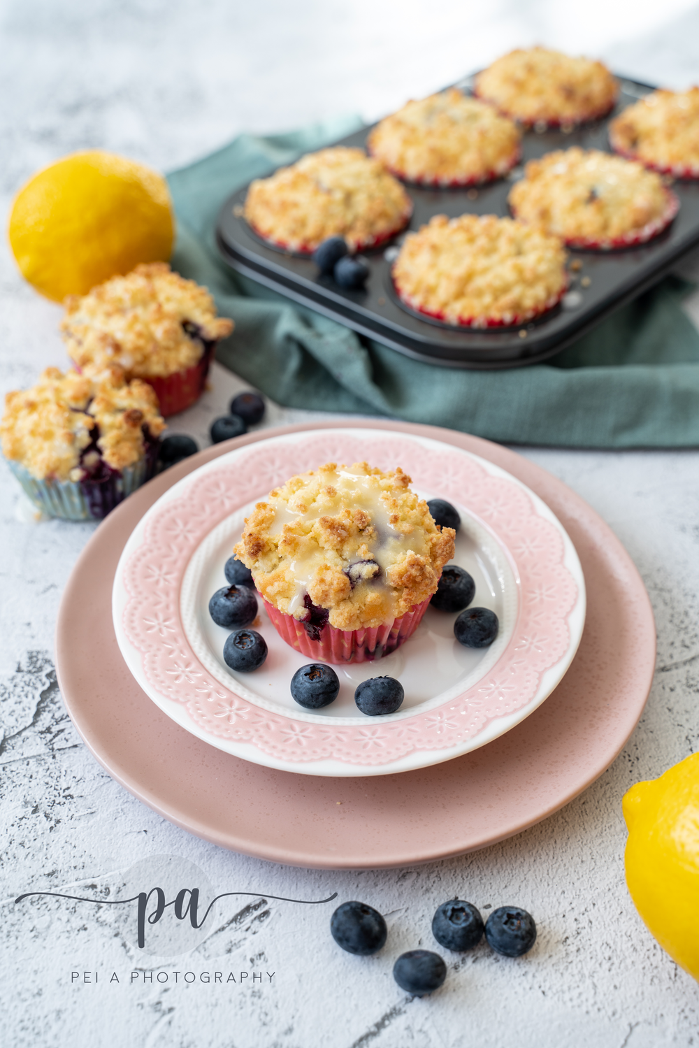 Fresh blueberry muffin with crumb topping on pink plate with scattered berries and lemons taken by Melbourne food styling photographer.