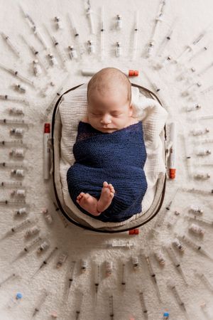 Overhead view of sleeping newborn in navy wrap on textured white circular backdrop.