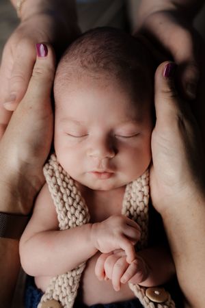 Sleeping newborn wearing a knit outfit while being held in gentle hands.