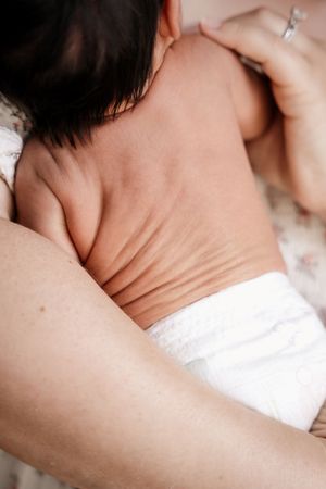 Close-up of a newborn baby lying on its stomach in a diaper, cradled in a parent's arms.