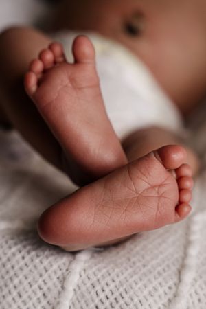 Close-up of newborn baby feet crossed over a white knit blanket, showing tiny toes and soft skin texture.