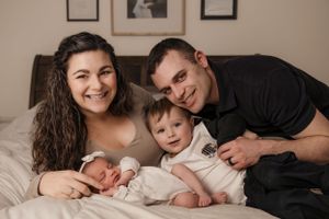 Indoor family lifestyle portraits on neutral bedding with natural lighting.