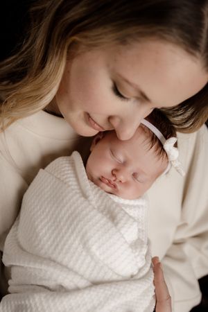 Tender moment between parent and newborn baby dressed in white. Portland, Maine