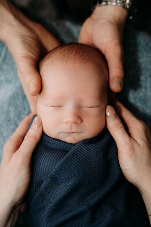 Close up details of sleeping newborn baby wrapped in navy blue knit blanket.