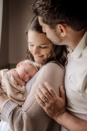 Tender family moment with newborn baby wrapped in knit blanket being held close.