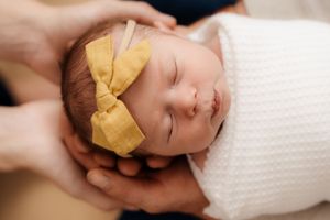 Close-up of a sleeping newborn wearing a yellow bow headband resting on white fabric.