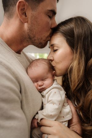 Intimate family moment with parents sharing tender kisses with their newborn baby.