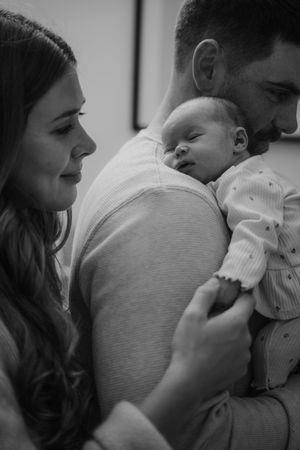 Black and white portrait of tender family moment with newborn in soft lighting.