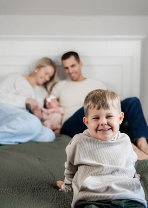 Child in cream sweater smiling while sitting on dark green couch.