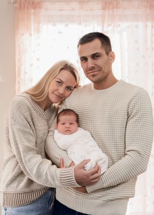 Family wearing matching cream sweaters holding newborn in bright room.