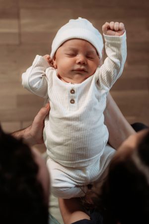 Baby wearing white ribbed onesie against wooden floor background.