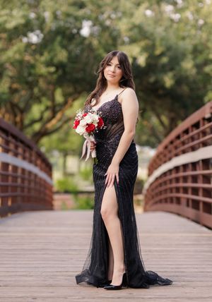 Woman in black sequined gown with slit holds red and white bouquet on wooden bridge outdoors.