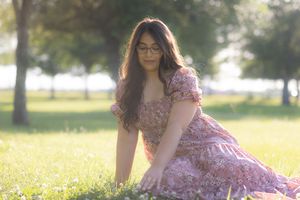 Outdoor portrait of model sitting on grass and lightly touching the grass in front of her.