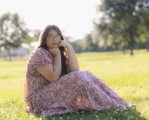 Outdoor portrait of model sitting on grass at golden hour while her face rest on her hands.
